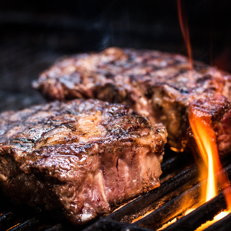 Hereford beef steaks cooking over flames on a barbecue